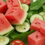 Fresh watermelon, cucumber, cherry tomatoes, and leafy greens arranged for summer salad.
